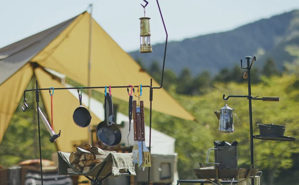 Camping scene with a yellow tent and camp kitchen gear hung from colorful carabiner clips on a metal rack.